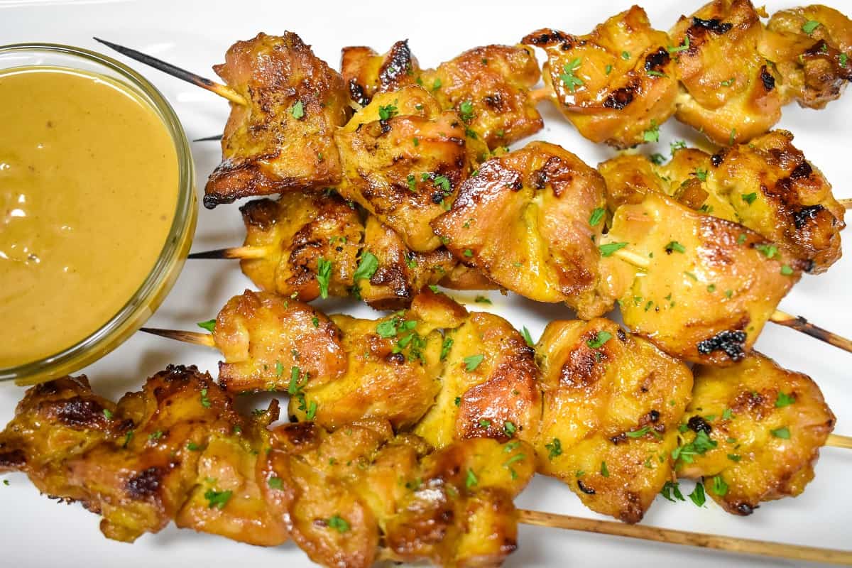 Chicken satay served with peanut sauce on a white platter.