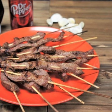 Dr Pepper marinated steak skewers arranged on an orange plate.