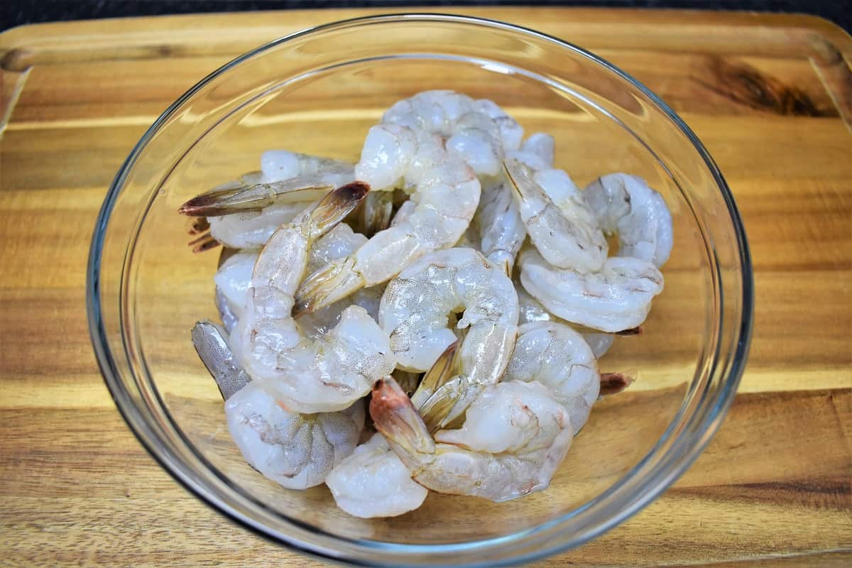 Peeled large shrimp in a clear bowl displayed on a wood cutting board.