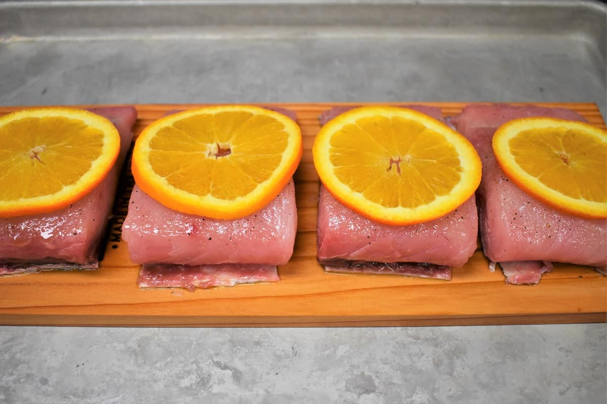 Four mahi mahi fillets arranged on a cedar plank and topped with an orange slice.