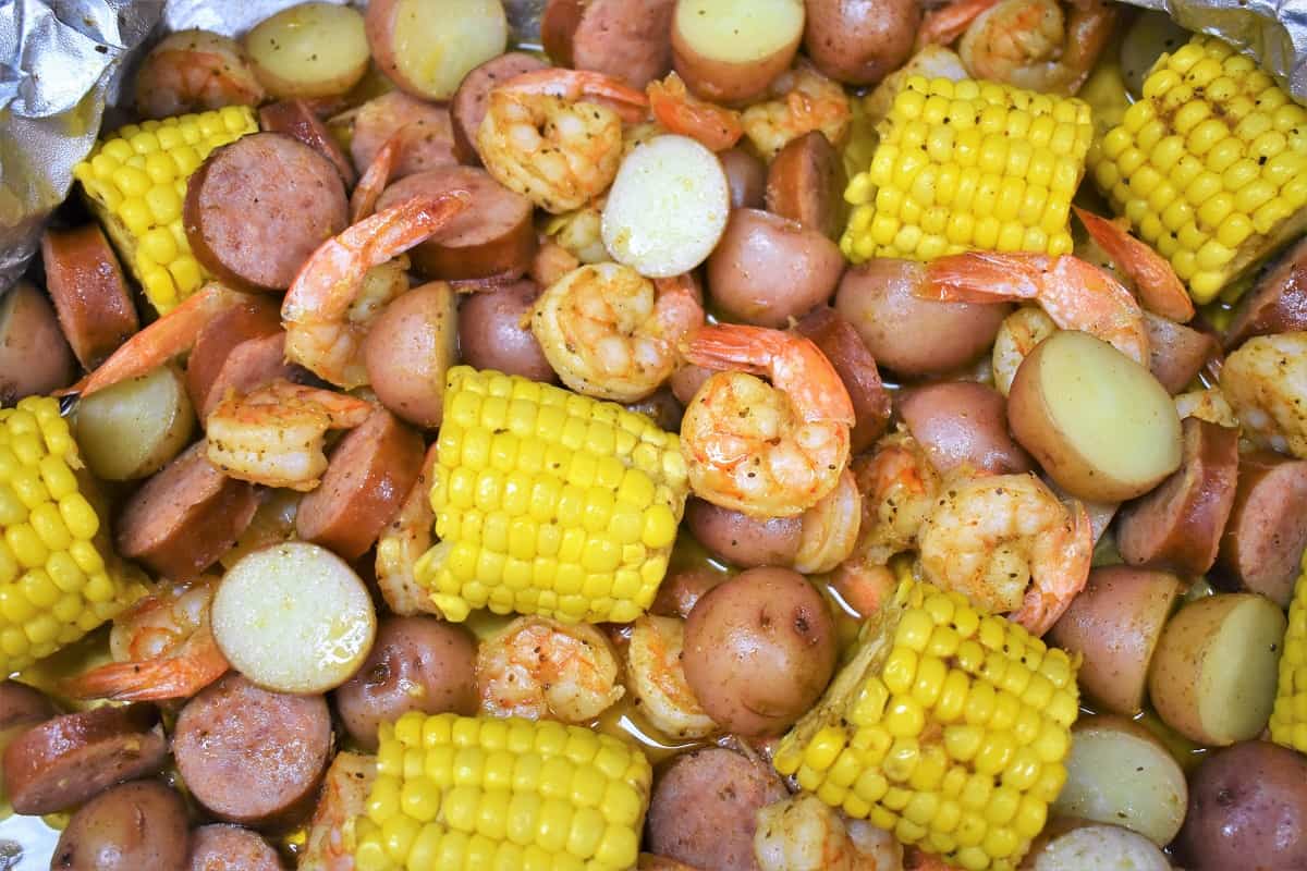 A close up of sausage, shrimp, corn and potatoes in an open aluminum foil pack.
