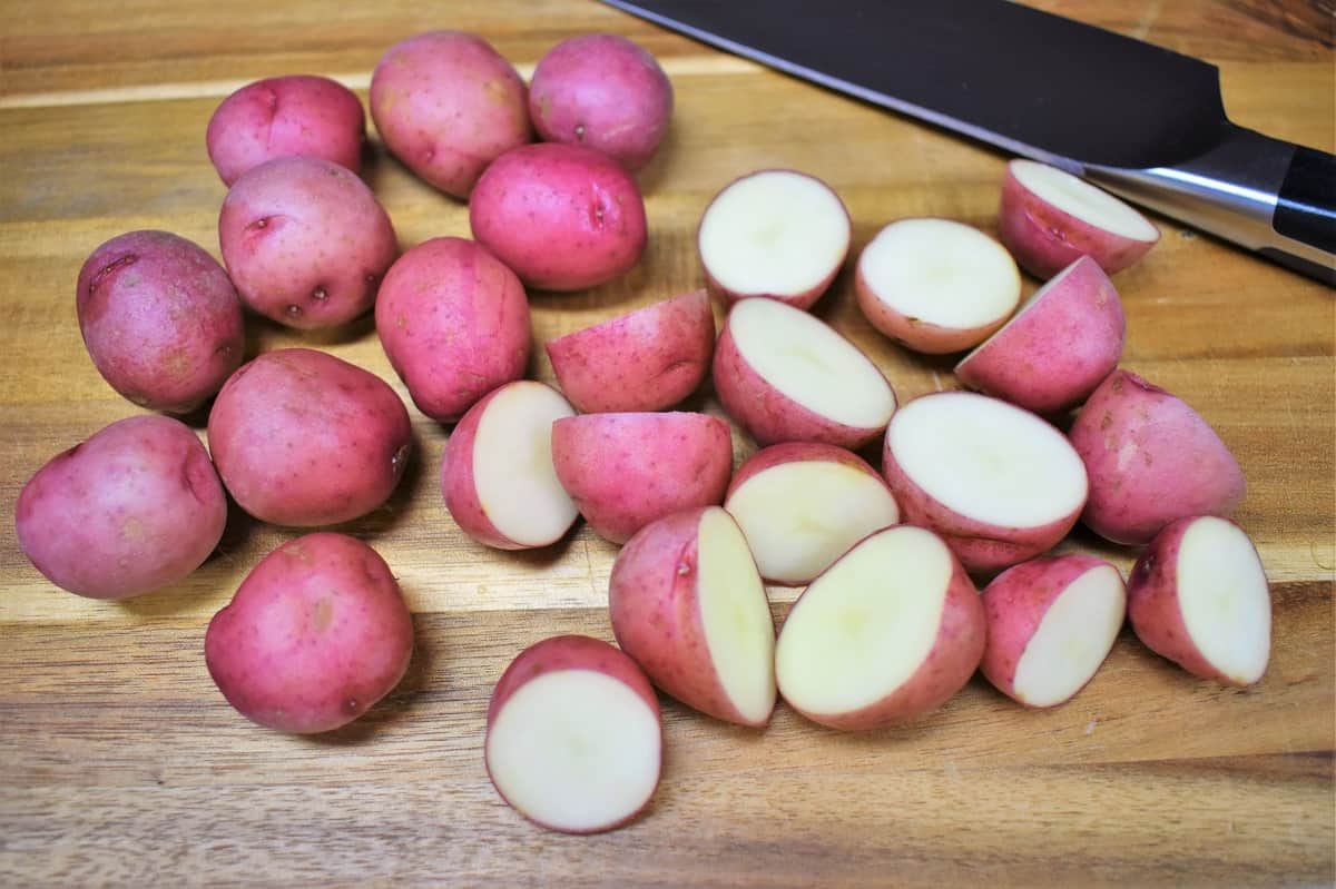 Small red potatoes, cut in half and displayed on a wood cutting board.