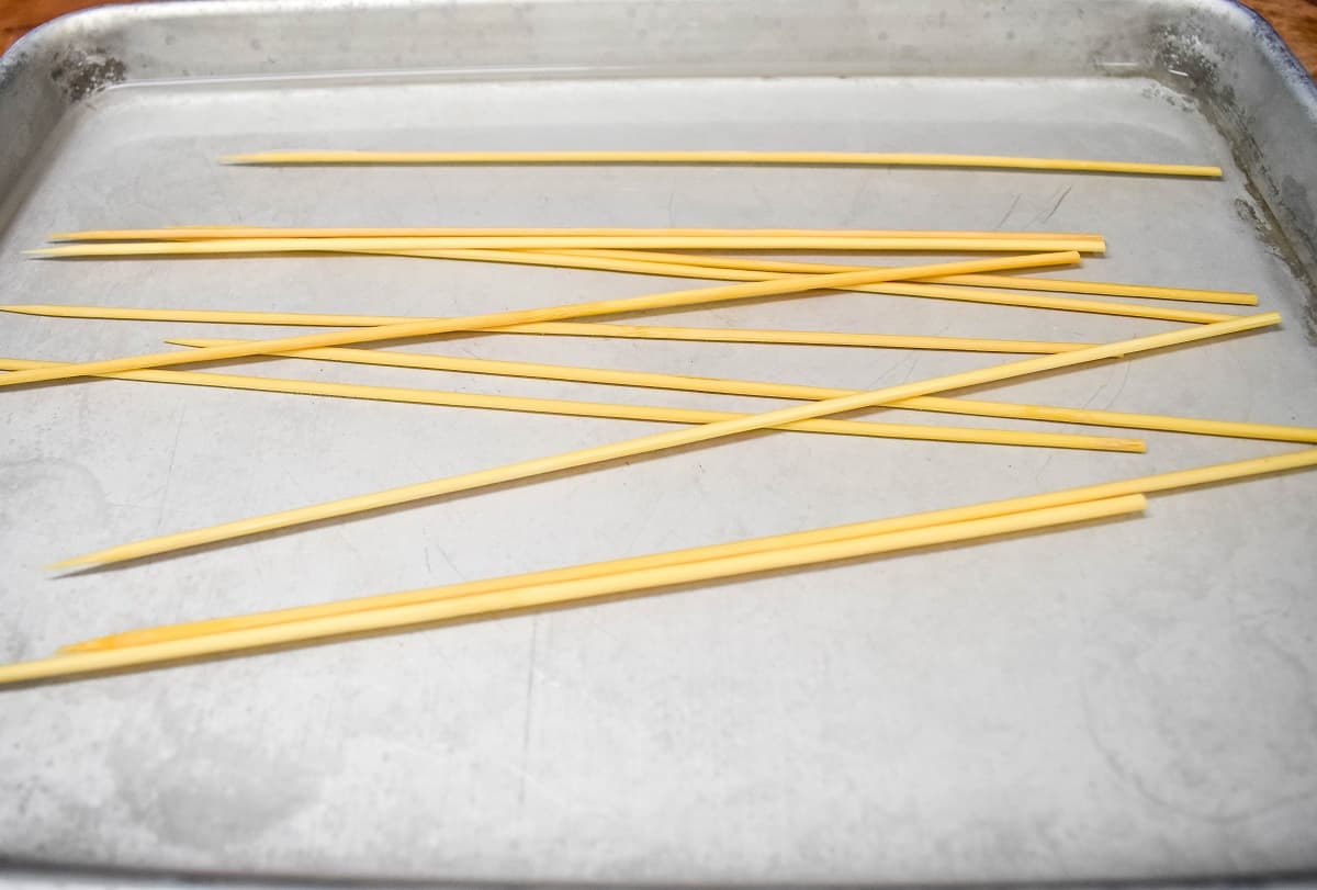 Several bamboo skewers covered with water in a metal sheet pan.