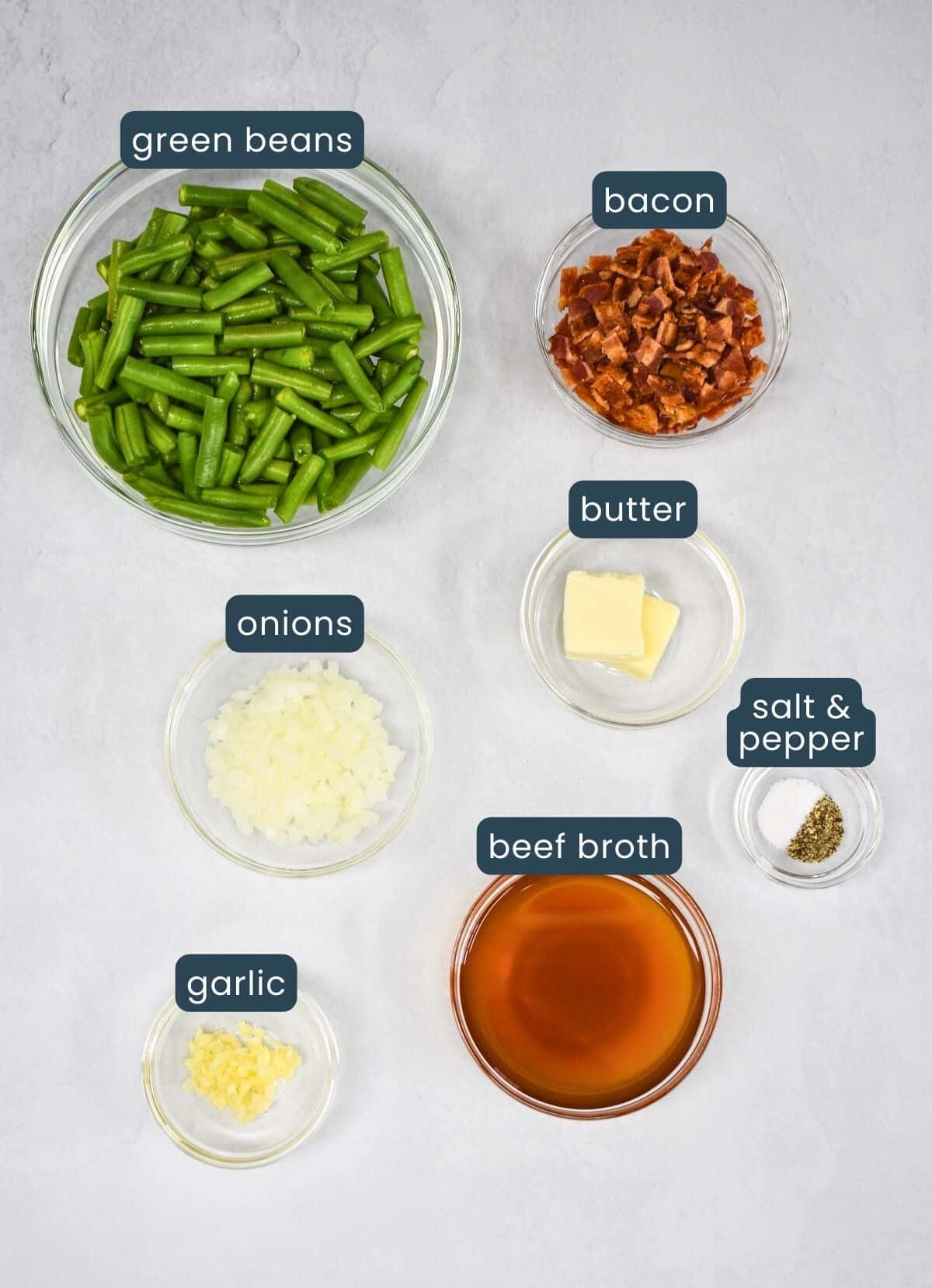The ingredients for the recipe prepped and arranged in glass bowls on a white table, with each labeled with small, white and blue letters.