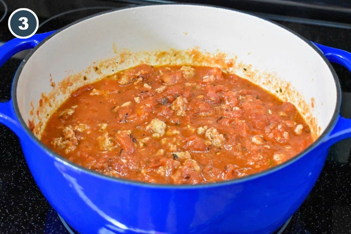 The sausage red sauce cooking in a large blue pot.