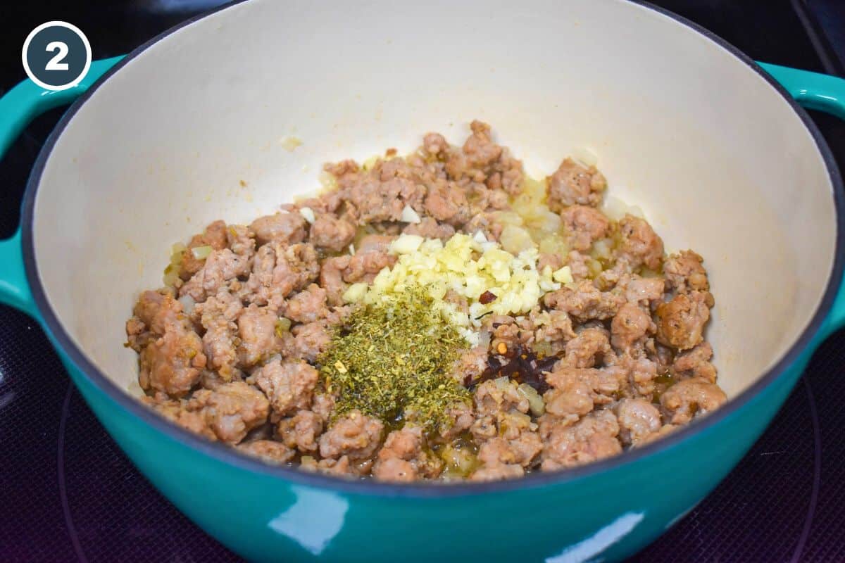 Minced garlic and herbs added to sausage in a pot.