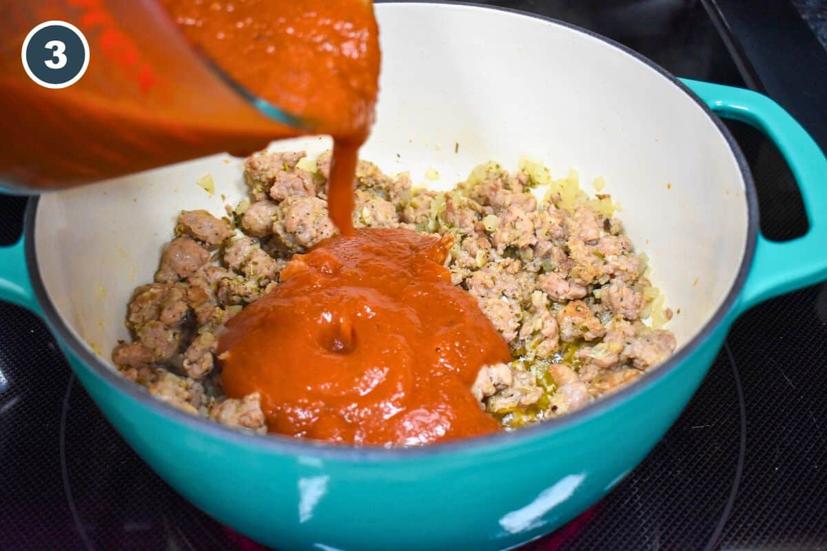 Pasta red sauce being added to sausage in a pot.