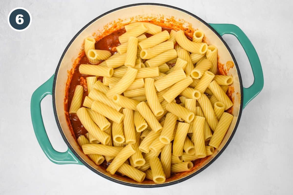 Cooked rigatoni noodles on a pasta red sauce in a teal pot.