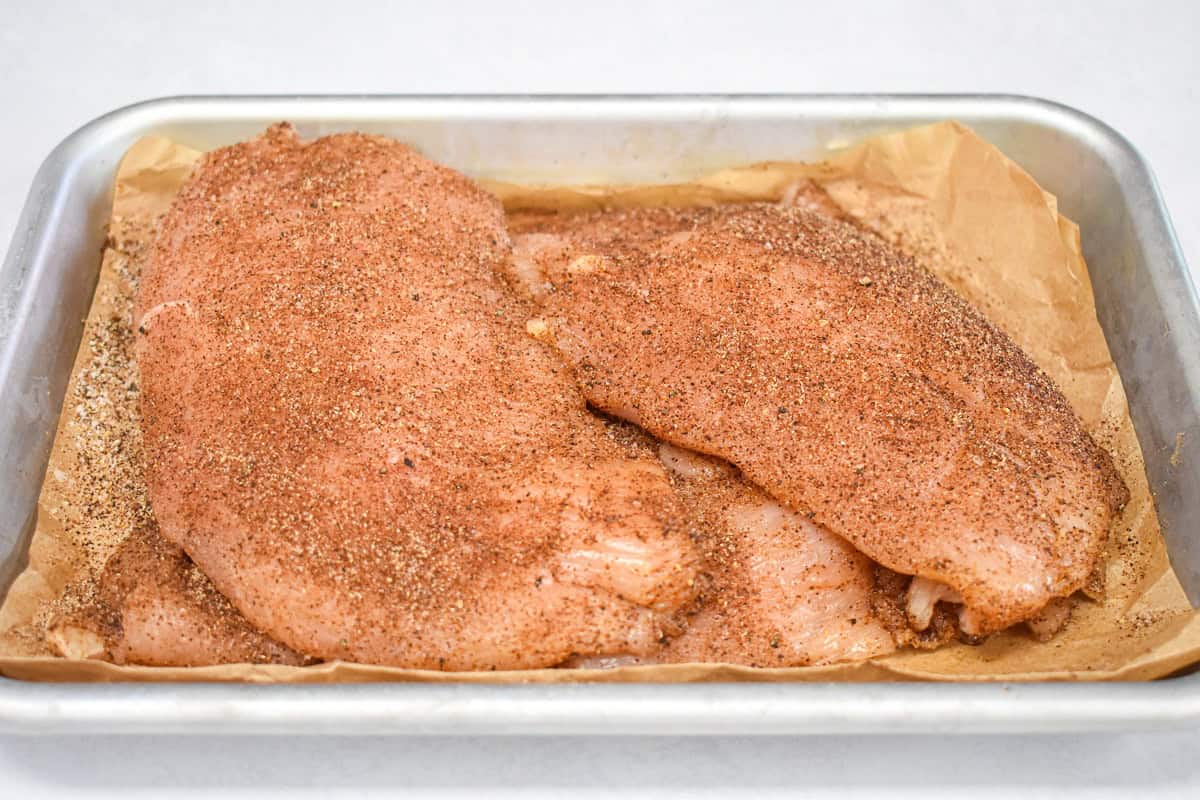 Seasoned boneless, skinless chicken breast in a small pan lined with parchment paper.