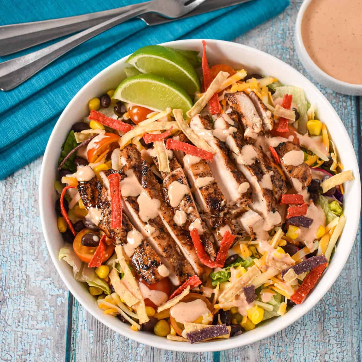 The grilled chicken southwest salad finished and dressed with the chipotle dressing in a white bowl.