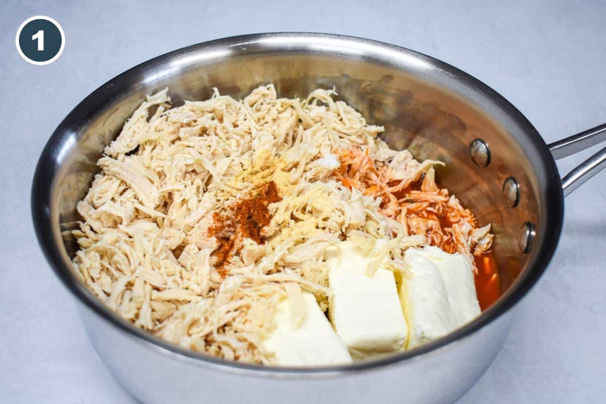 Shredded chicken, cream cheese, hot sauce, and spices in a saucepan.