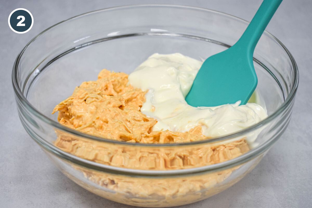 The chicken mixture and sour cream in a large bowl before mixing with a blue spatula.