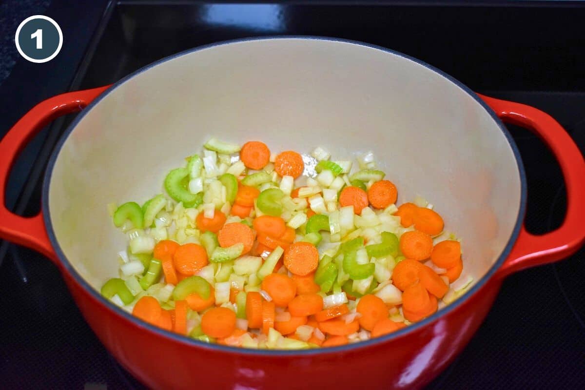 Diced onions, carrots, and celery sautéing in a large, red and white pot.