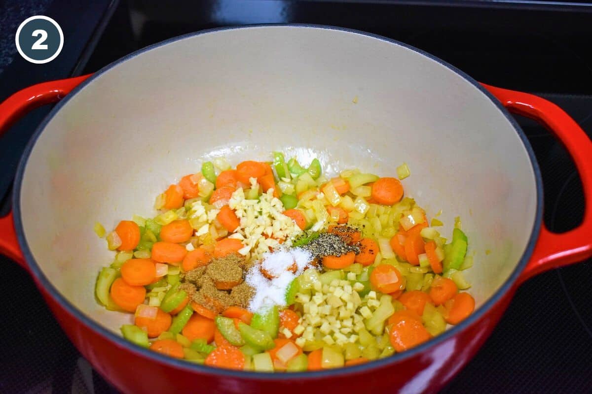 Diced onions, carrots, celery, garlic, and spices sautéing in a large, red and white pot.