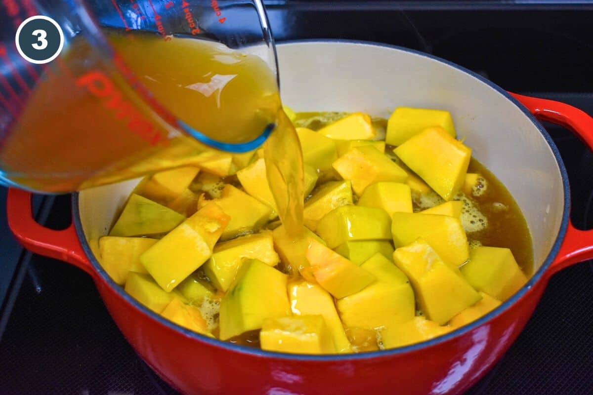 Vegetable broth being added to the vegetables and cut pumpkin in a red and white pot.