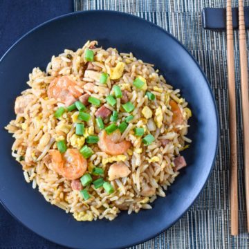 The finished house special fried rice served on a black plate with a black linen to the left and chopsticks to the right.