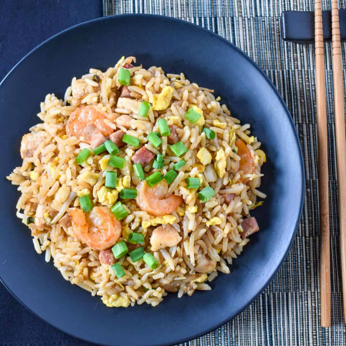 The finished house special fried rice served on a black plate with a black linen to the left and chopsticks to the right.