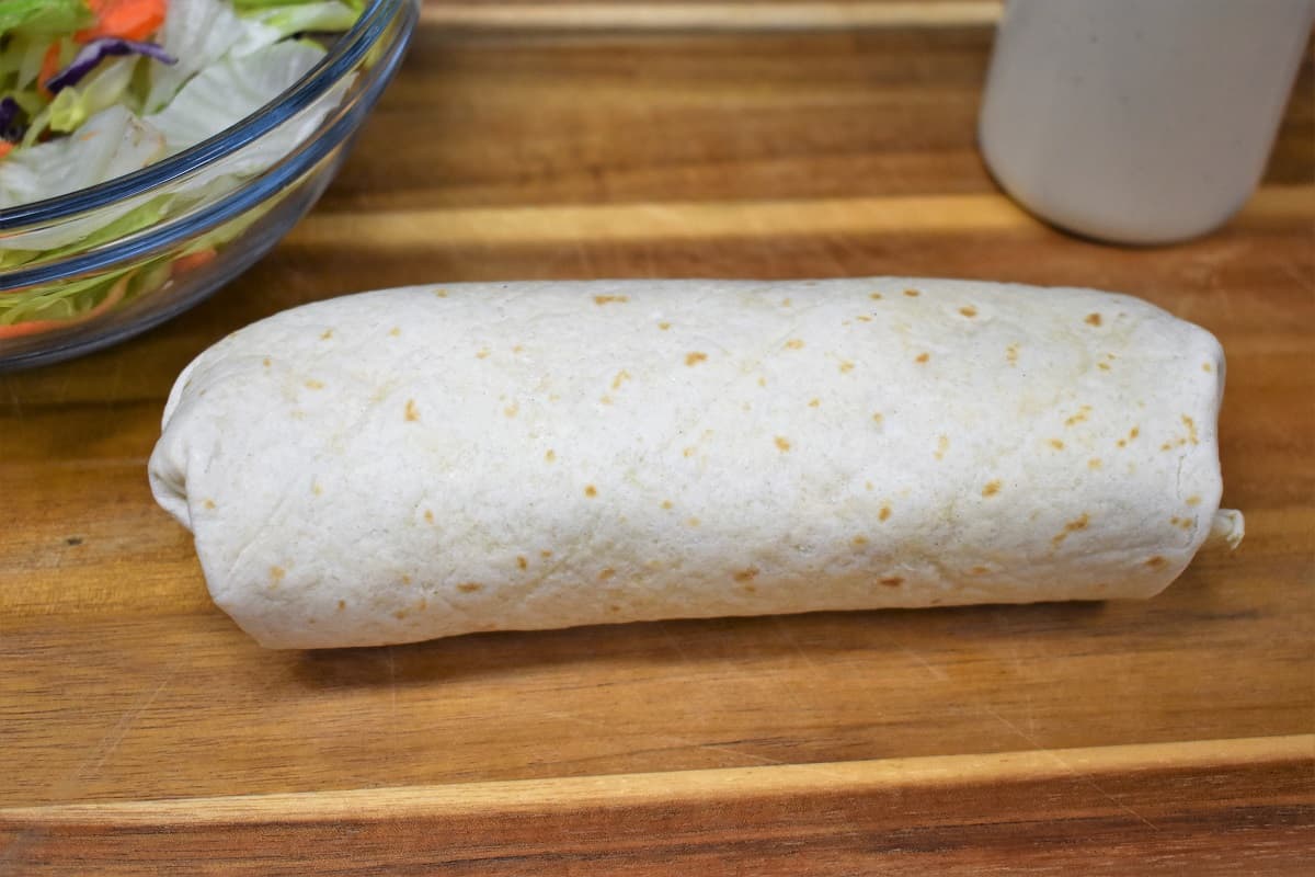 A Rolled Buffalo Chicken Wrap on a wood cutting board