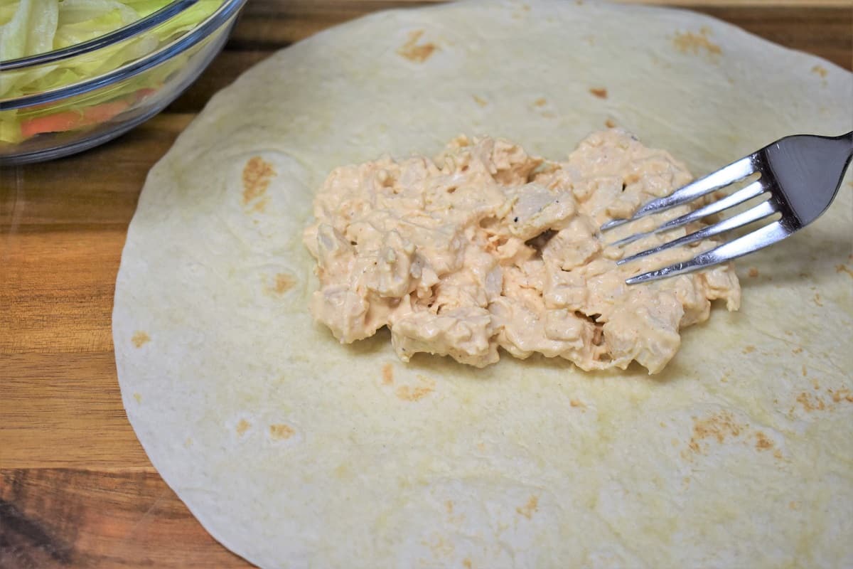 Buffalo Chicken salad being spread on a Large Flour Tortilla