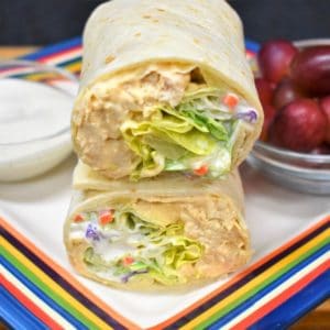 A Buffalo Chicken Wrap cut in half and stacked, served with ranch and grapes.