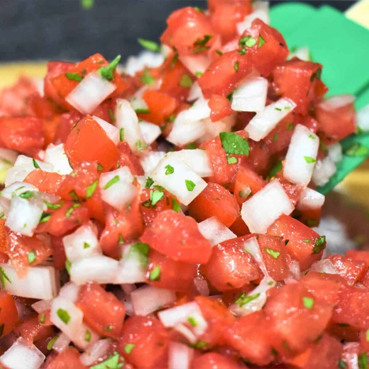 The garden fresh salsa in a large, glass bowl being stirred with a green spatula.