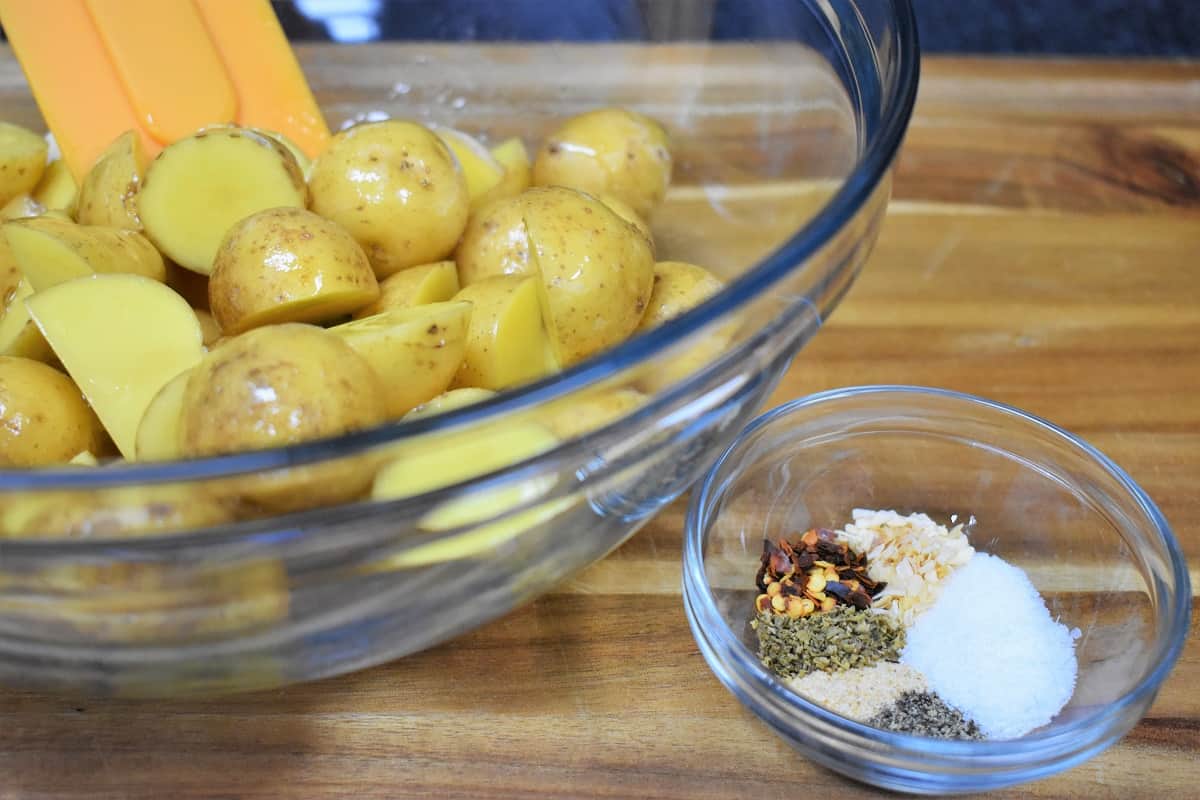 Honey gold potatoes cut in half in a clear glass bowl with a small clear bowl with the seasoning mix next to it.