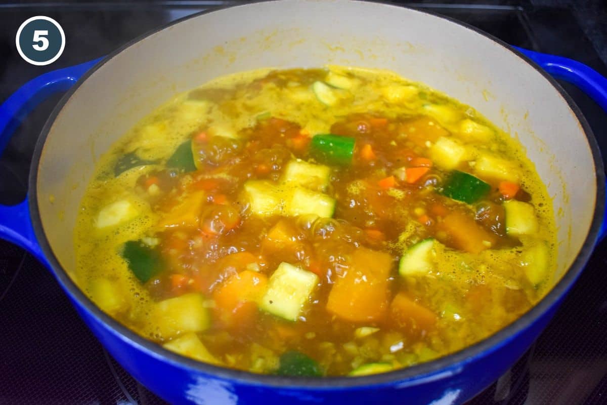 Vegetables simmering in broth in a blue and white pot.