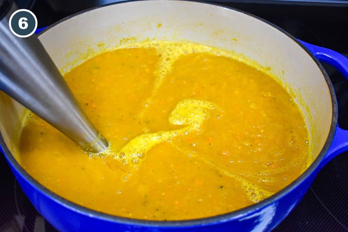 An immersion blender pureeing the soup in the pot.