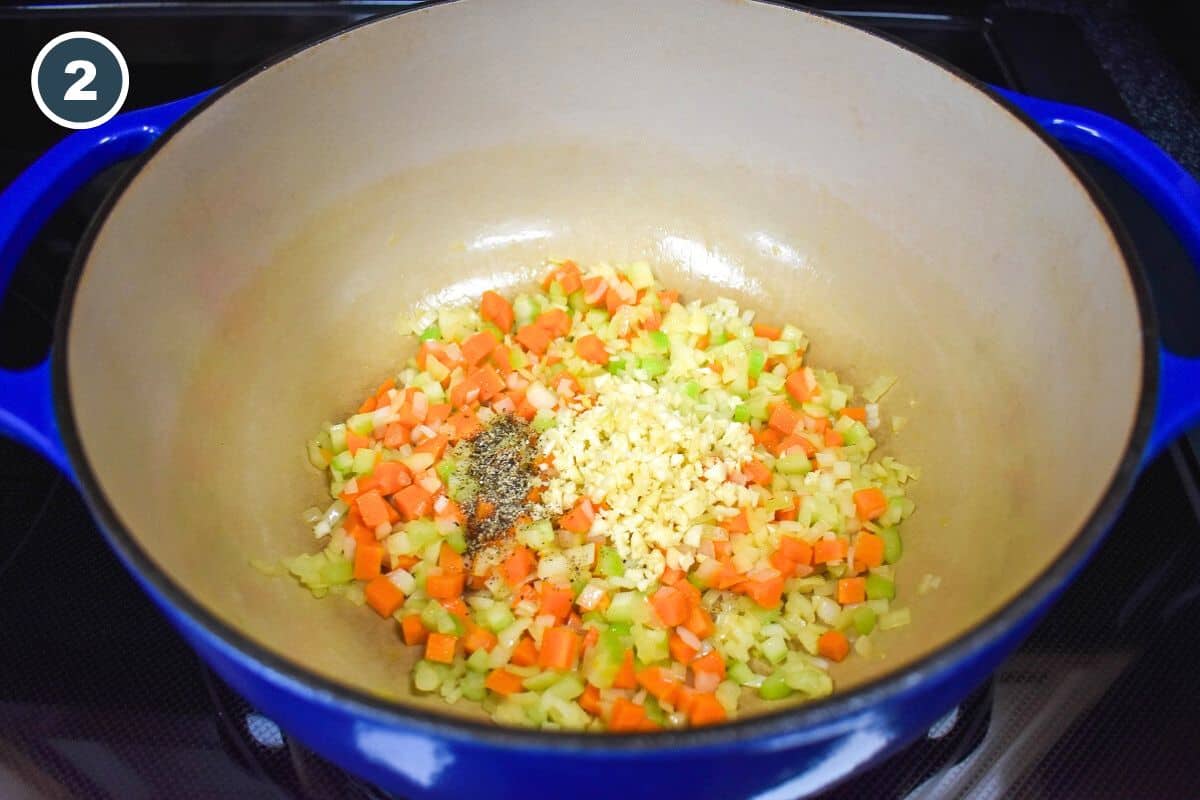 Minced garlic and spices added to the diced onions, carrots, and celery in a large, blue pot.