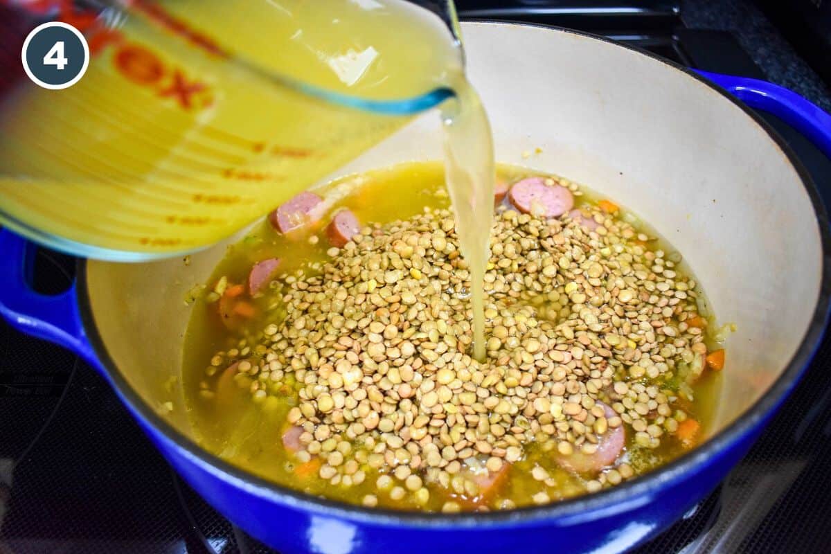 Chicken broth being added to lentils and other ingredients in a blue pot.