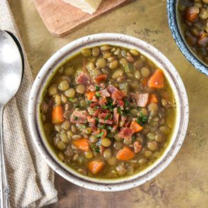 The bacon lentil soup served in a small bowl and garnished with bacon bits and chopped parsley.