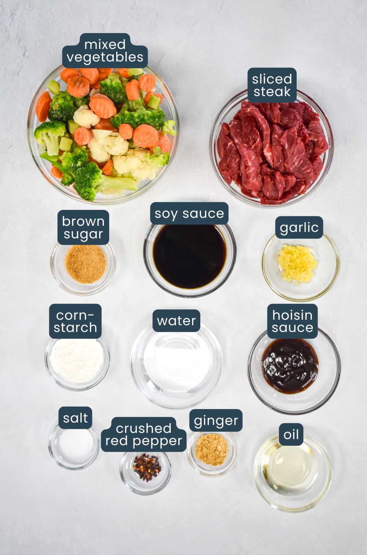 The ingredients for the stir fry prepped and arranged in glass bowls with each ingredient labeled with blue and white letters.