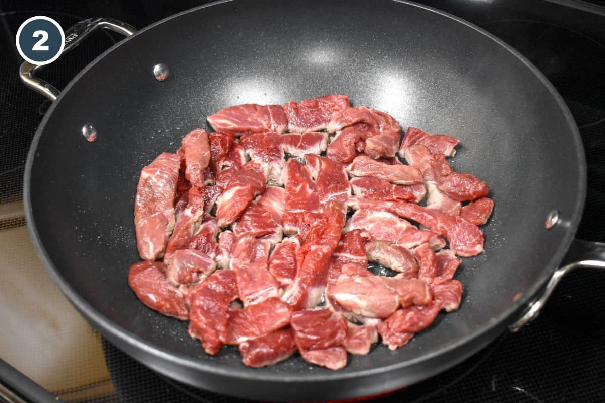 Raw steak strips arranged in a large, black saute pan.