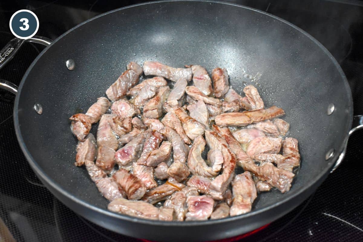 Browned steak strips arranged in a large, black saute pan.