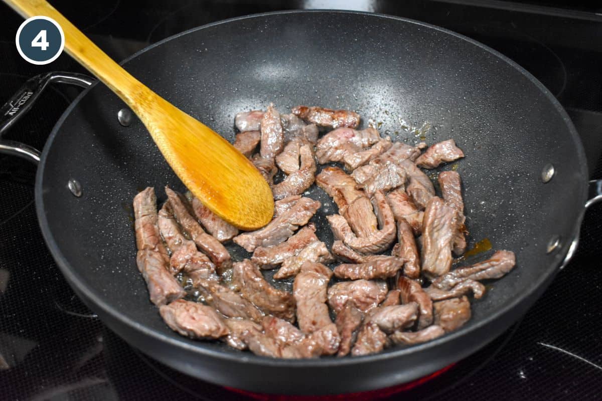 Steak strips in a large saute pan stirred with a wooden spoon.