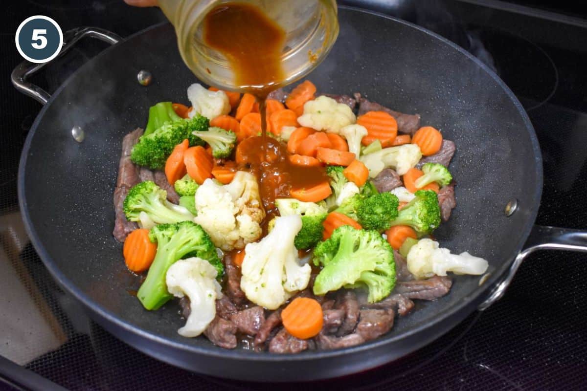 Stir fry sauce being added to steak strips and mixed vegetables in a large pan.