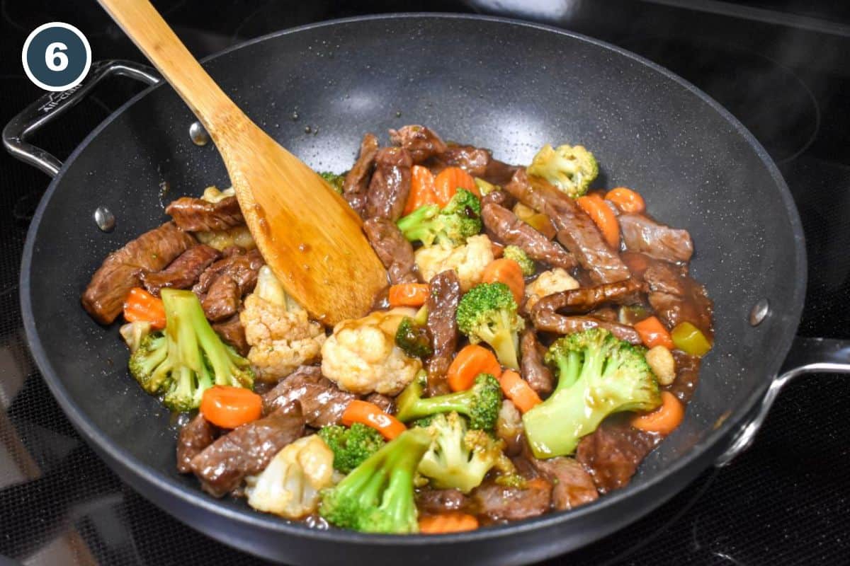 The stir fry in a large pan with a wooden spoon.