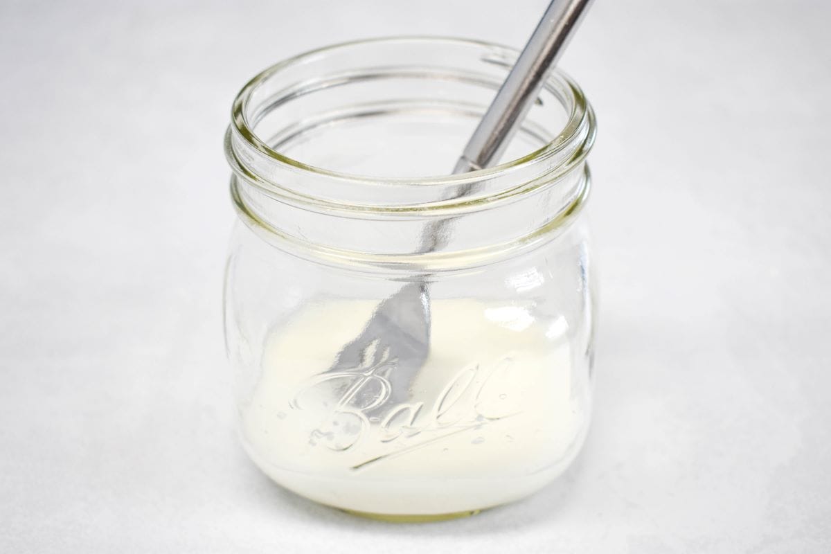 Cornstarch and water with a fork in a small mason jar, set on a white table.