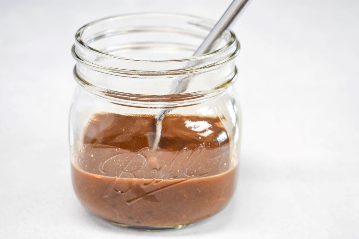 Stir fry sauce and a fork in a small mason jar set on a white table.