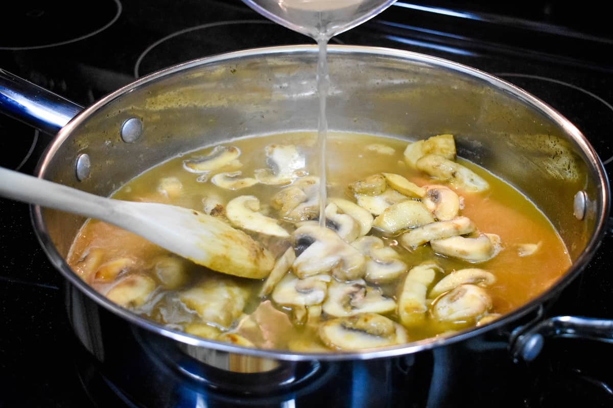 Chicken broth being added to sliced mushrooms in a large skillet.