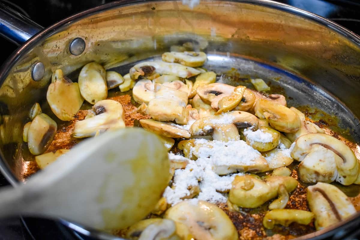 Sliced mushrooms and flour being cooked in a large skillet.