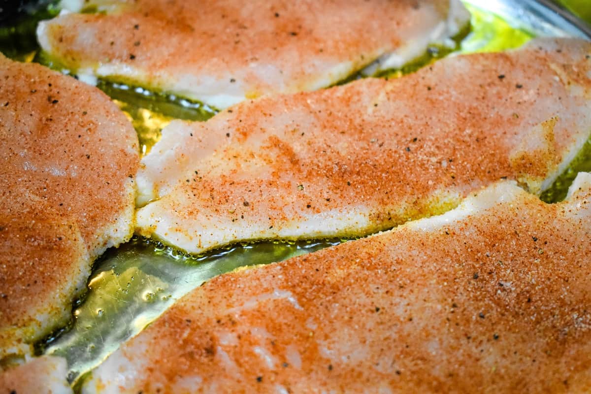 Thin chicken breasts cooking in a large, metal skillet.