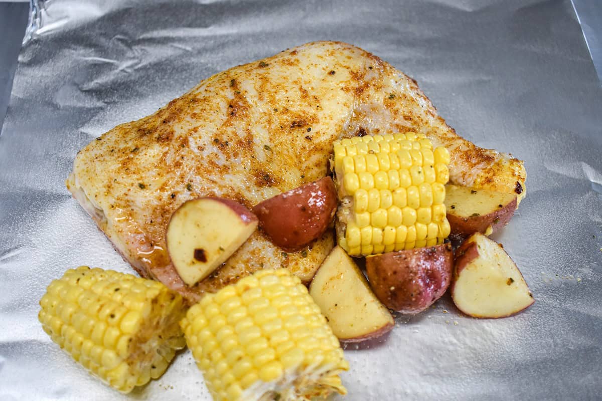 The chicken, corn cobs, and cut potatoes on aluminum foil.