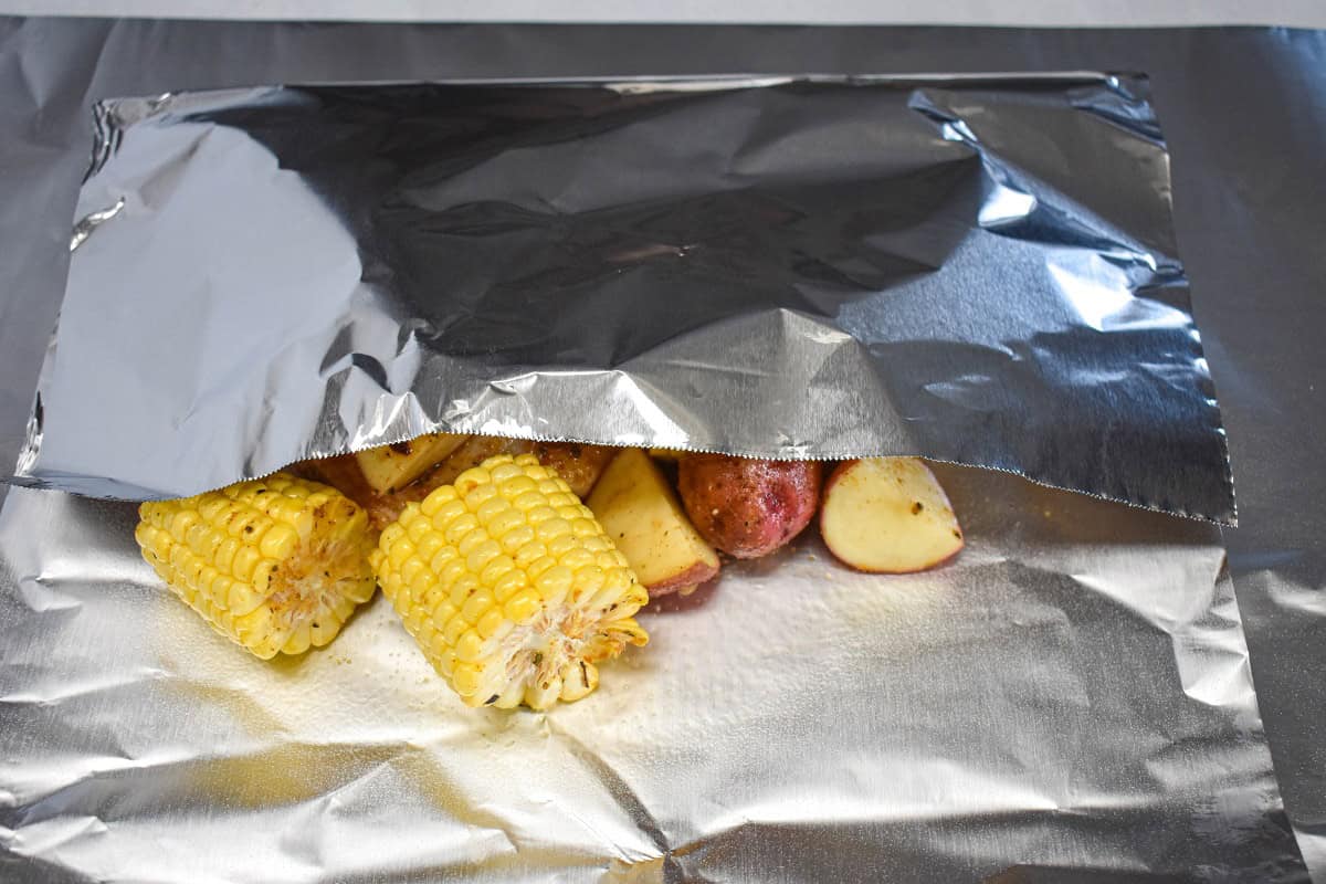 The foil covering the ingredients with only corn cobs and a couple of potatoes visible.
