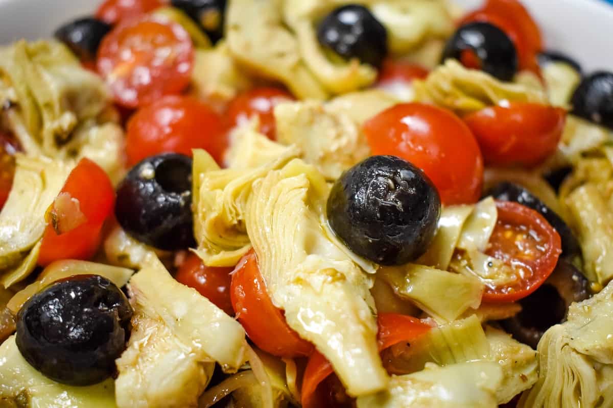 A cold salad with quartered artichokes, grape tomatoes, black olives and sliced onions coated with an oil and vinegar dressing.