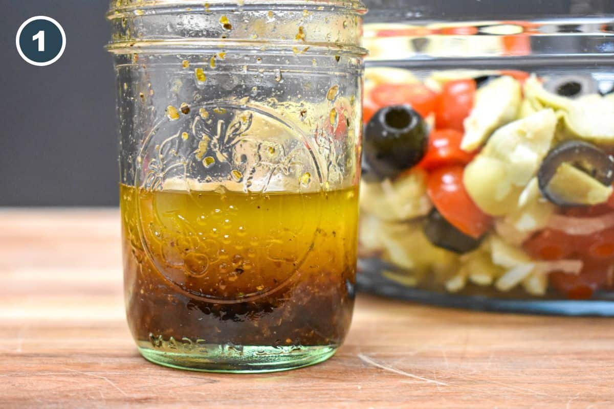 The dressing for the salad in a small canning jar, with the artichoke salad in a glass bowl in the background.