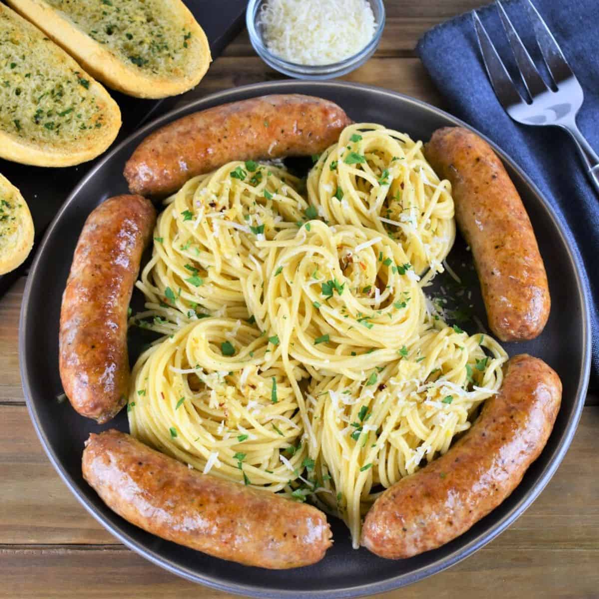 A large platter of spaghetti aglio e olio with Italian sausage arranged around the pasta.