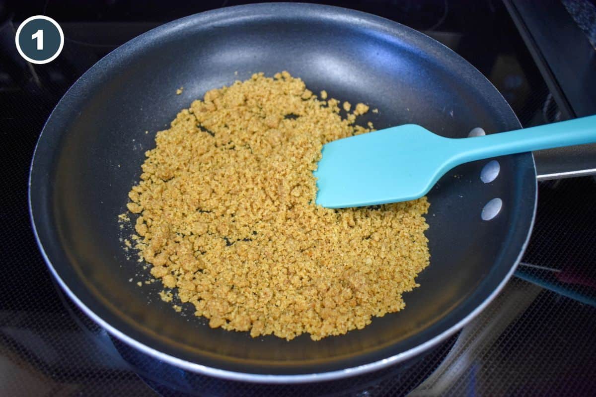 Toasting breadcrumbs in a skillet with a blue spatula for the casserole topping.