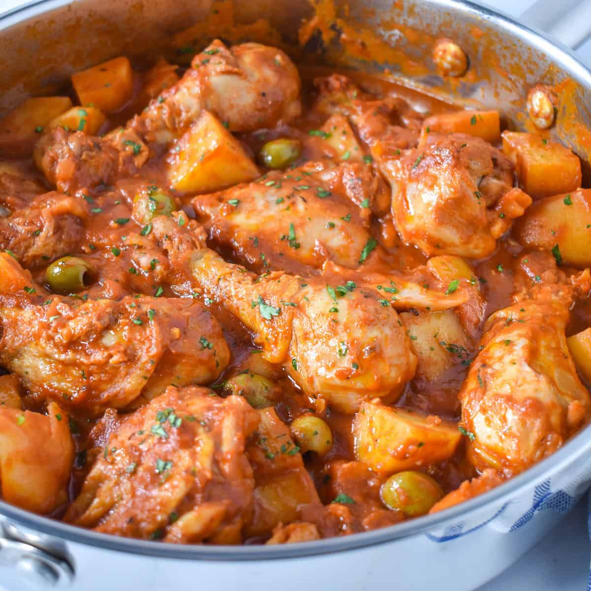 Fricase de pollo in a large saute pan garnished with parsley.