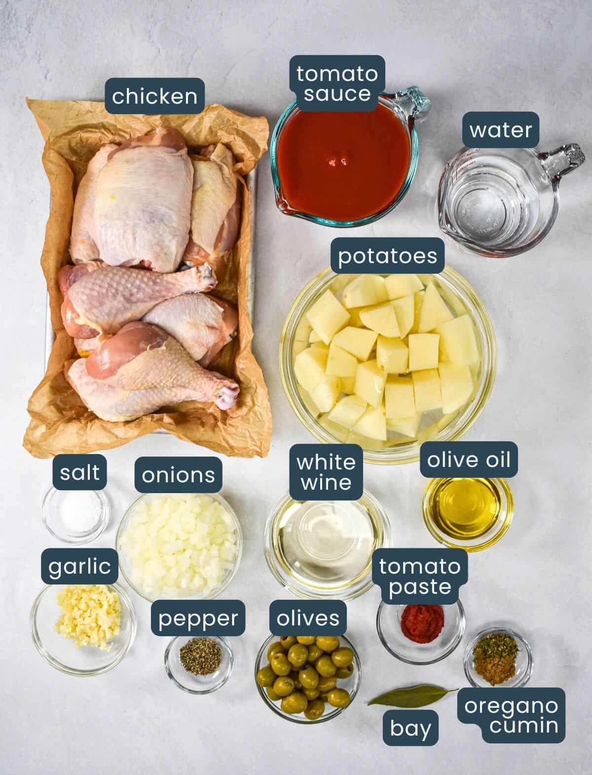 The ingredients for the dish prepped and arranged in glass bowls on a white table. Each ingredient is labeled in blue with white letters.